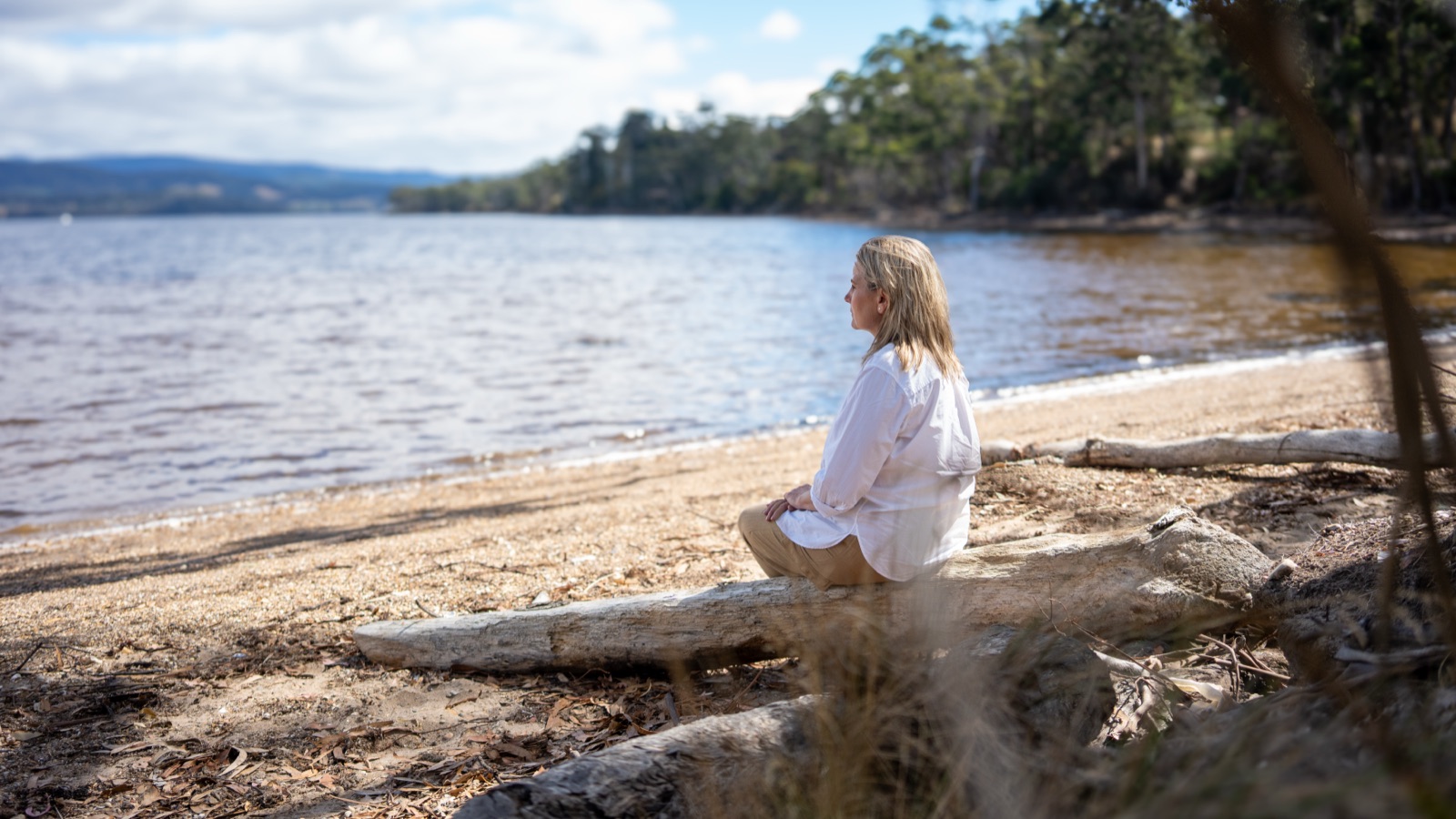 Annica seated on driftwood, looking out toward the water — prospect and possibility